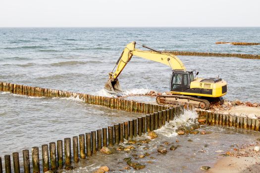 excavator during the construction of a breakwater by the sea on autumn day