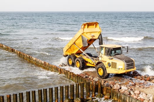 heavy truck during the construction of a breakwater by the sea on autumn day