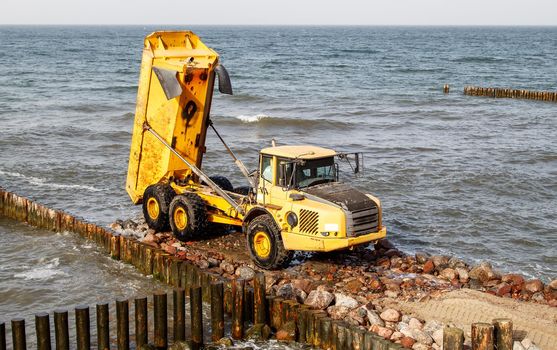 heavy truck during the construction of a breakwater by the sea on autumn day