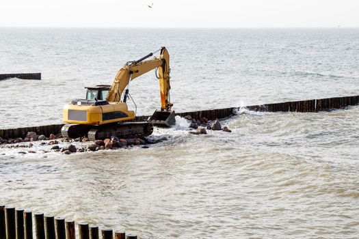 excavator during the construction of a breakwater by the sea on autumn day