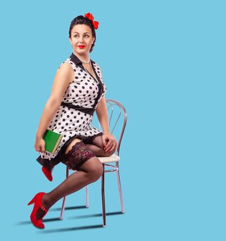 young brunette woman holds book sitting on a chair in studio. pinup style