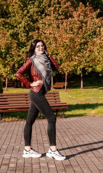 young girl in brown jacket and black jeans standing on the alley in city park on sunny autumn day