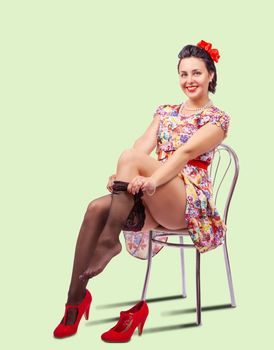 woman straightens her stocking while sitting on a chair in studio. pinup style