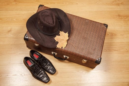 set of men's felt hat with a yellow maple leaf, black shoes and a suitcase on a wooden floor