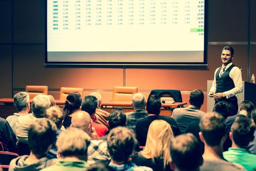 Speaker giving a talk in conference hall at business meeting event. Rear view of unrecognizable people in audience at the conference hall. Business and entrepreneurship concept.