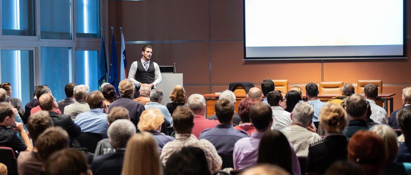 Speaker giving a talk in conference hall at business meeting event. Rear view of unrecognizable people in audience at the conference hall. Business and entrepreneurship concept.