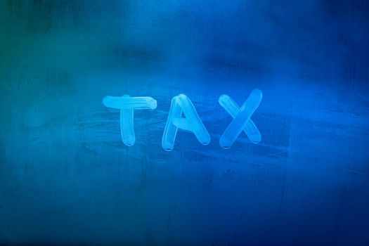 word tax hadwritten on night wet window glass surface with blue colors in blurry background