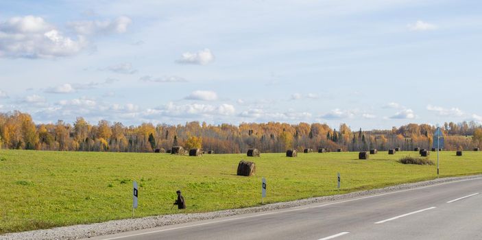 Road between fields with hay bales in autumn. Agricultural field with sky and clouds. The nature of agriculture. Straw in the meadow. Rural natural landscape. The harvest of grain and the harvest.