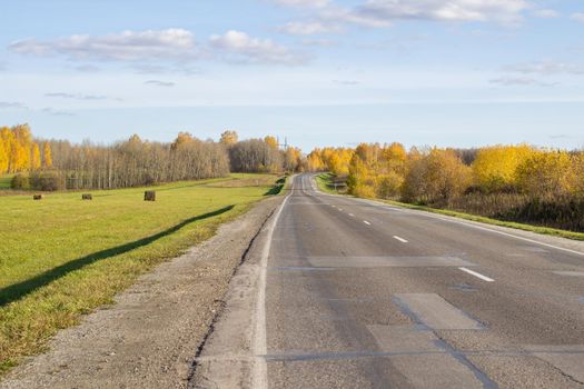 Road between fields with hay bales in autumn. Agricultural field with sky and clouds. The nature of agriculture. Straw in the meadow. Rural natural landscape. The harvest of grain and the harvest.