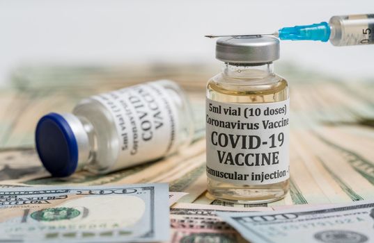 Covid-19 coronavirus vaccine with hypodermic syringe needle sitting on pile of cash to suggest payment to get the vaccination