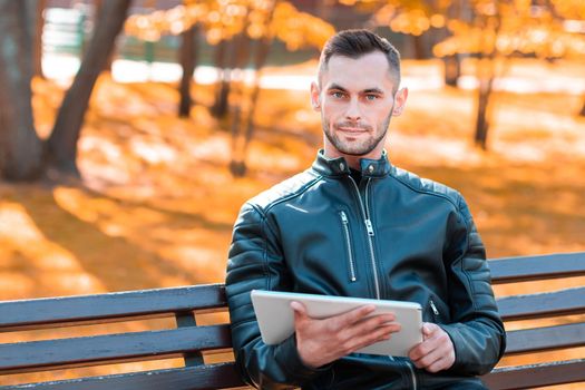 Handsome Young Man Sitting on the Bench and Using Big White Tablet PC at the Beautiful Autumn Park