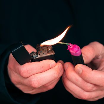 Setting Fire to the Firecracker. Man in Black Clothes Lighting Up the Petard. Firing Up the Pyrotechnics with a Black Gasoline Lighter Outdoors