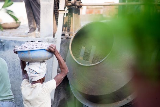 Jaipur, Rajasthan, India - circa 2020 : zoomed in shot of indian underprivleged construction workers carrying sand, cement, stones and water on their head to load into a mixer to make concrete for the making of infrastructure real estate, homes and offices in India. Shows the manual labor and hard work employed by the real estate and construction industry with lack of safety in the country of India