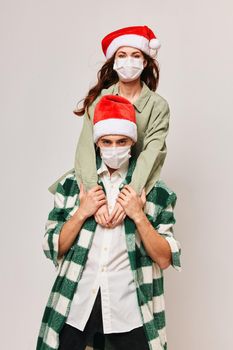 A woman in a holiday hat sits on the shoulders of a man in a medical mask. High quality photo