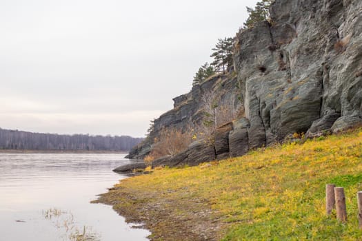 Beautiful, wide autumn river among forests and rocky shore. A calm and quiet place with autumn colors. Reflection of clouds in the water in good weather