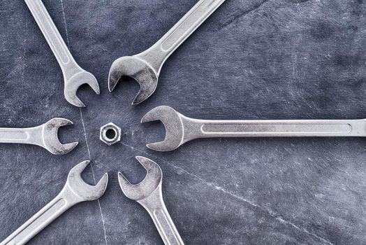 Circle of spanners or wrenches surrounding a nut on a grunge stone surface, top view