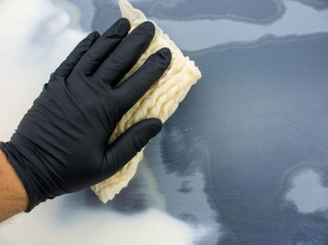 the hand of the auto-painter in a black glove holds a special napkin for dusting the surface of the car. preparation for painting the car