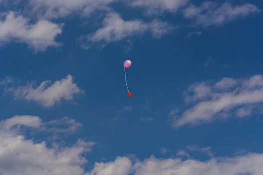 Pink balloon with ribbon and greeting card in front of blue sky