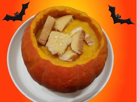 Spicy pumpkin soup with ginger and onions, served in pumpkin with pumpkin. Pkin oil, seeds and croutons on the Halloween background. This is a german version of pumpkin soup