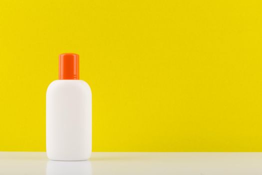 Minimalistic still life with unbranded sunscreen lotion for safe tanning on white table against yellow background with copy space. High quality photo