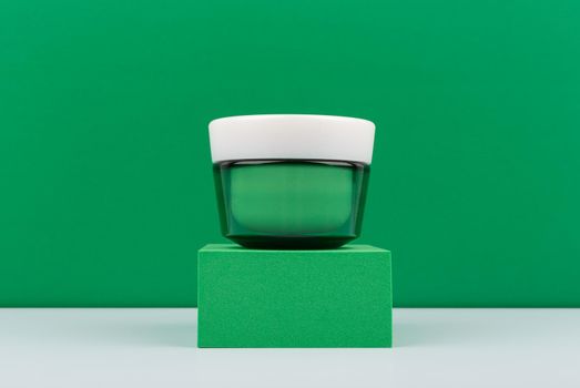 Simple still life with green cream jar against green background with space for text. Concept of organic or luxury anti aging skincare with natural ingredients