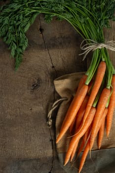 Fresh organic carrots with canvas on antique wooden table. Rustic kitchen concept. Banner, poster, mock up. Grunge, vintage, rustic style