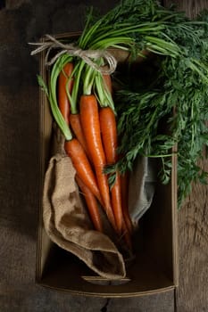 Fresh organic carrots in a box with canvas on antique wooden table. Rustic kitchen concept. Banner, poster, mock up. Grunge, vintage, rustic style