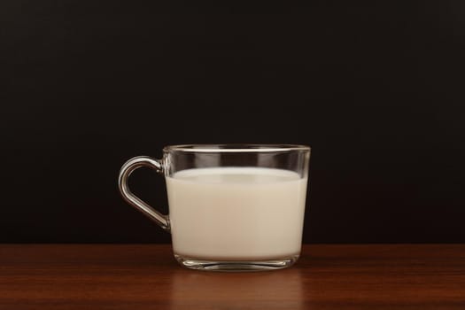 Minimalistic still life with a cup of milk on brown wooden table against black background. High quality photo