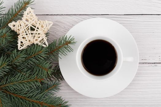 Simple horizontal flat lay with a cup of coffee on white rustic table decorated with Christmas tree and toy star. Concept of winter season and hot drinks