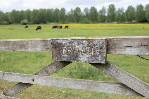 Sign Private on wooden gate in front of green rural field