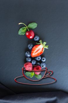 Summer fruits, berries and mint in chalk painted cup of tea on black background. Conceptual healthy, vitamin, dietary food. Vegan, vegetarian and detox food and drinks. Menu mock up for cafe, poster concept