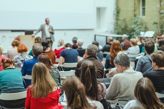 Male speaker giving presentation in lecture hall at university workshop. Audience in conference hall. Rear view of unrecognized participant. Scientific conference event. Copy space on whitescreen.