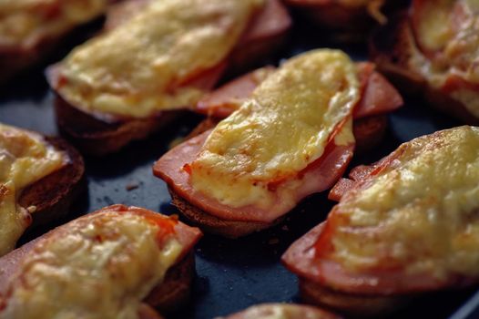 Many baked hot sandwiches with ham and cheese lie on a tray in a row. View from above.