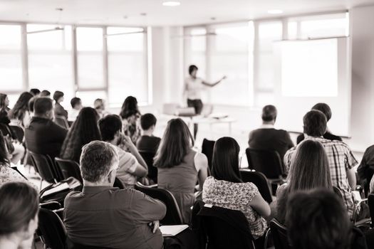 Business and entrepreneurship symposium. Speaker giving a talk at business meeting. Audience in conference hall. Rear view of unrecognized participant in audience.