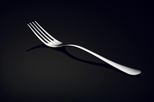 A white metal fork lies on a black glass with a reflection. A simple kitchen item for advertising. 