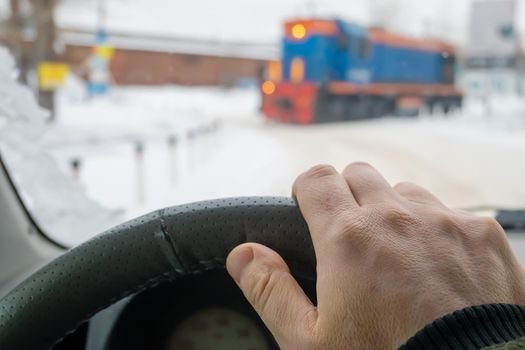 the driver's hand on the steering wheel of a car that has stopped, waits and passes the locomotive of the train that blocked the road