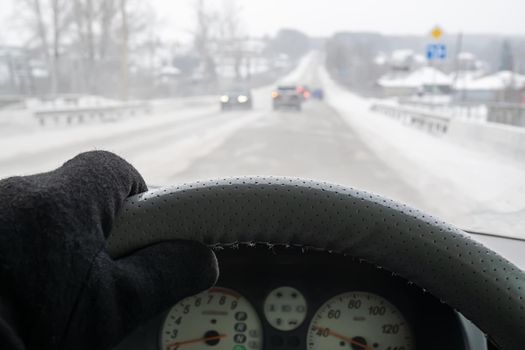 the hand of the driver behind the wheel of a car in a warm glove, which is driving in winter on a snow-covered slippery road before climbing a hill