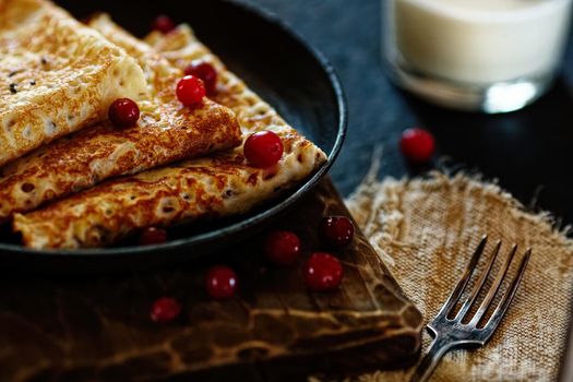 Delicious home-cooked food. Pancakes in a frying pan with cranberry berries and milk. National Russian cuisine. Ready lunch. Rustic style.