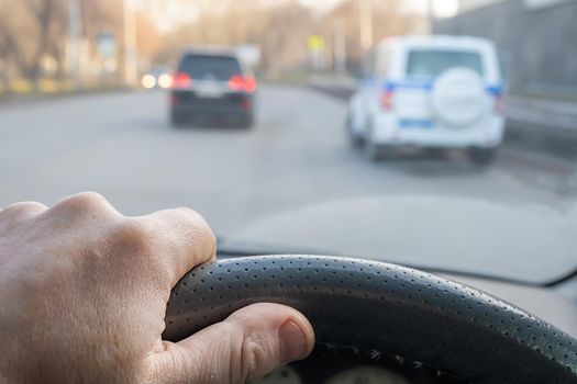 the driver's hand on the steering wheel of a car that is driving on the road behind a police car