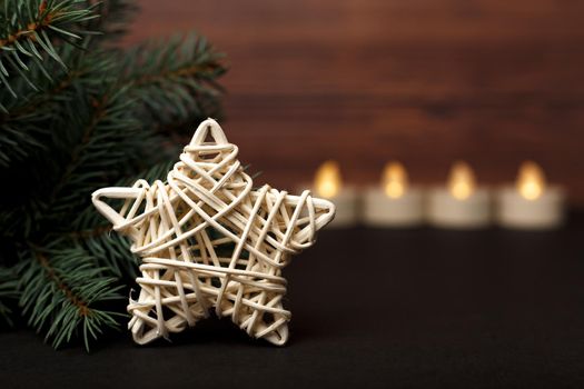 Close up of a white hand made rotang decorative star near the Christmas tree with candles at the background and against brown wooden wall