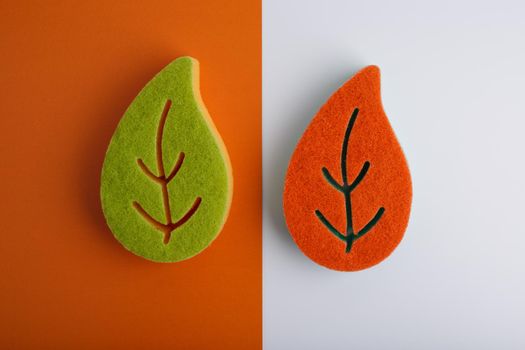 Top view of colorful leaf shaped sponges for home, kitchen, bathroom and and dishes cleaning on orange and white background