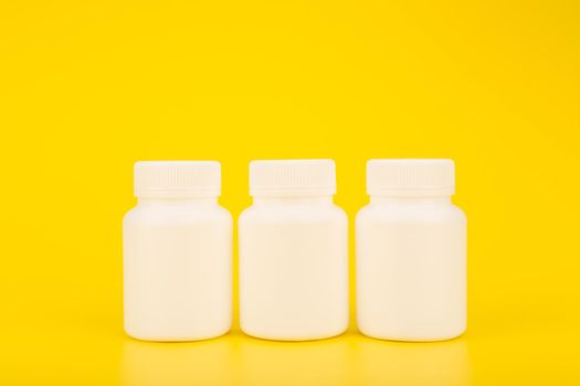 Creative minimalistic still life with three white plastic medication bottles in a row on yellow background. Concept of health and wellness