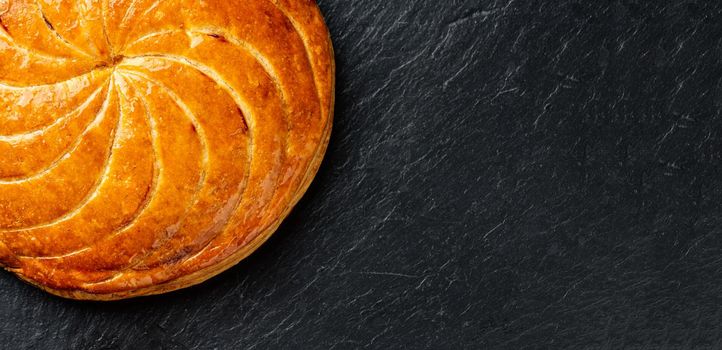 Epiphany cake or galette des rois in French on black slate background, panoramic crop with copy space