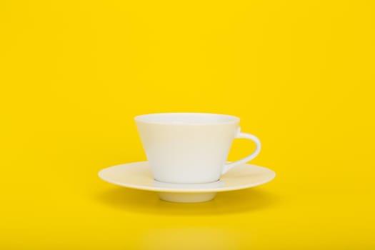 Minimalistic still life with white ceramic coffee or tea cup on a plate against bright yellow background with space for text. High quality photo