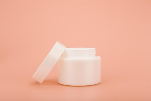 Minimalistic still life with white glossy opened cream jar on beige background with space for text