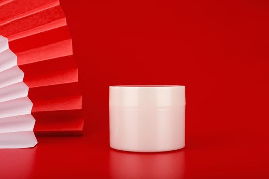 Minimalistic still life with white glossy cream jar on red background with red waver from the left side. Concept of skin care and beauty