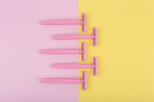 Top view of many pink razors on colored pink and yellow background