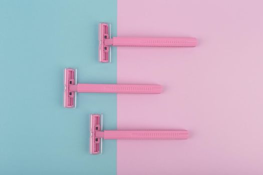Top view of three pink plastic razors on colored background. Hair removal concept