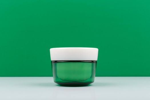 Still life with green cream jar against green background with space for text. Concept of organic skincare with natural ingredients
