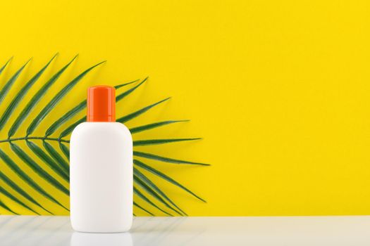 Sunscreen lotion in white jar with orange cap against yellow background with a palm. Concept of summer skin care 